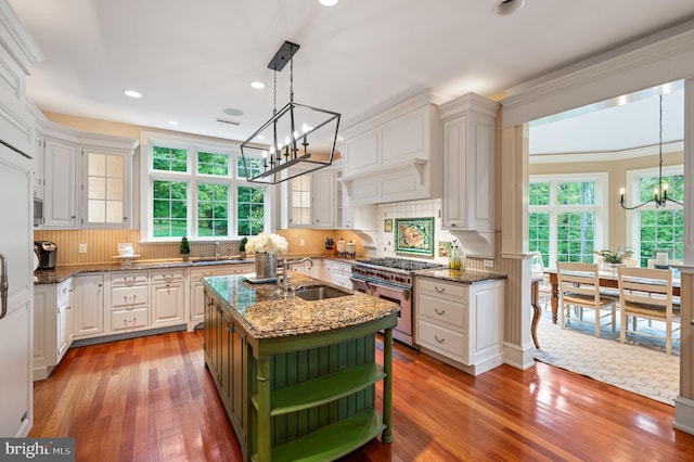 kitchen featuring a center island with sink, high end stainless steel range oven, sink, hardwood / wood-style flooring, and white cabinetry