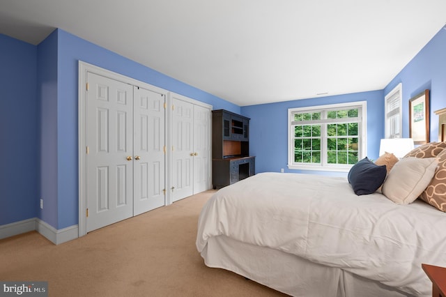 bedroom featuring light colored carpet and multiple closets