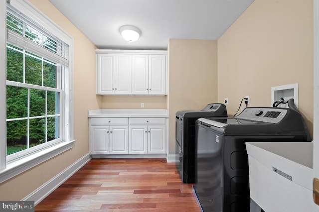 clothes washing area featuring cabinets, plenty of natural light, washer and dryer, and light hardwood / wood-style flooring