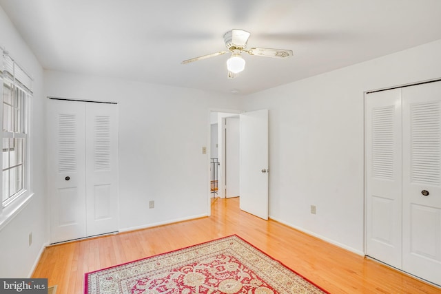 bedroom with wood-type flooring, multiple closets, and ceiling fan