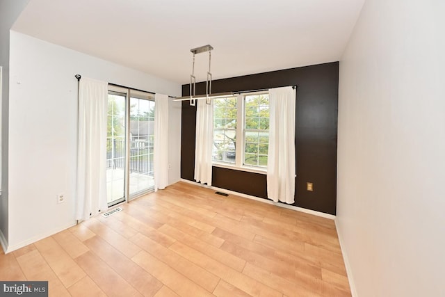 empty room with visible vents, light wood finished floors, a wealth of natural light, and baseboards