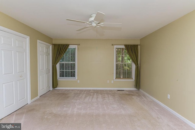 unfurnished bedroom featuring ceiling fan, two closets, and light carpet