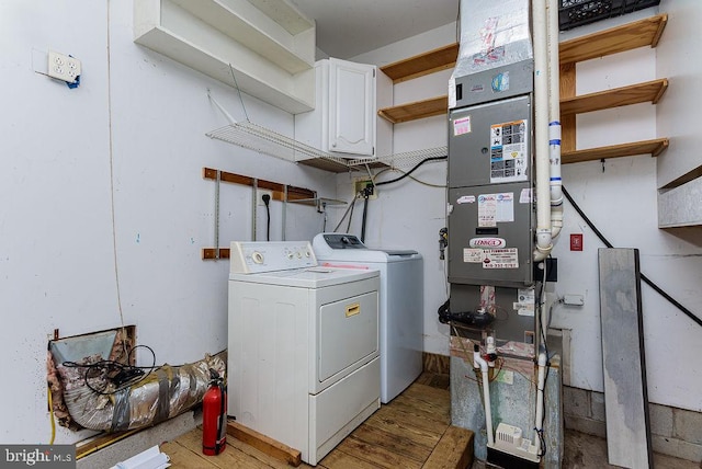 clothes washing area featuring washing machine and clothes dryer, light wood-type flooring, and cabinets