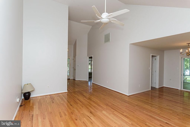 unfurnished living room with high vaulted ceiling, light wood-type flooring, and ceiling fan with notable chandelier