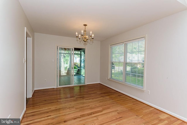 empty room with light wood-type flooring, a chandelier, and plenty of natural light