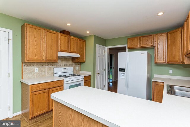 kitchen featuring tasteful backsplash, sink, kitchen peninsula, light hardwood / wood-style flooring, and white appliances