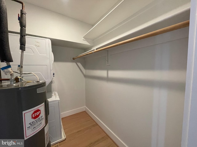 walk in closet with light hardwood / wood-style floors, stacked washer / dryer, and water heater