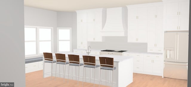 kitchen featuring light wood-type flooring, white refrigerator with ice dispenser, a kitchen island with sink, white cabinetry, and premium range hood