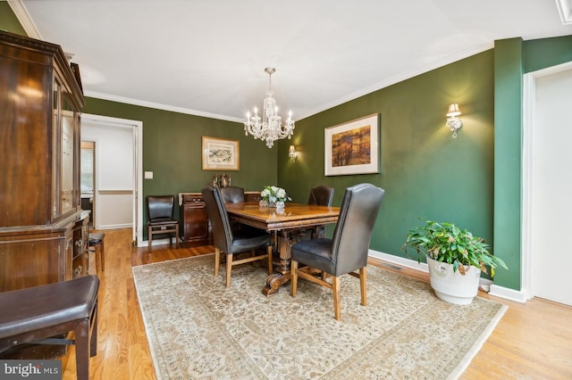 dining space with an inviting chandelier, light wood-type flooring, and ornamental molding