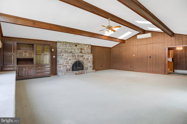 unfurnished living room with a wall mounted AC, ceiling fan, a fireplace, vaulted ceiling with skylight, and wooden walls