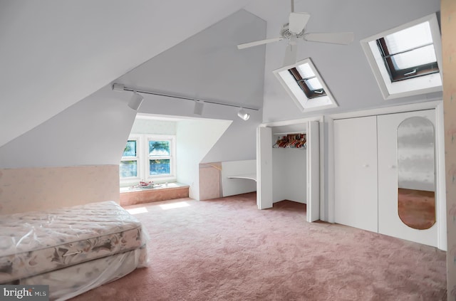 unfurnished bedroom featuring lofted ceiling with skylight, light carpet, two closets, and ceiling fan