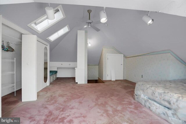 unfurnished bedroom with carpet flooring, vaulted ceiling with skylight, and ceiling fan