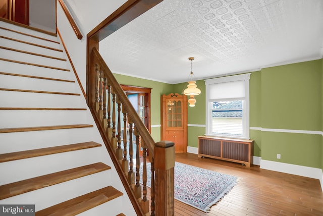 stairway with crown molding, radiator heating unit, and wood-type flooring