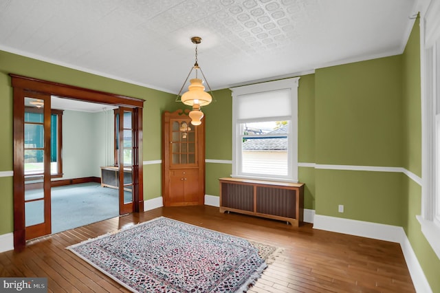 empty room with hardwood / wood-style floors, crown molding, and radiator