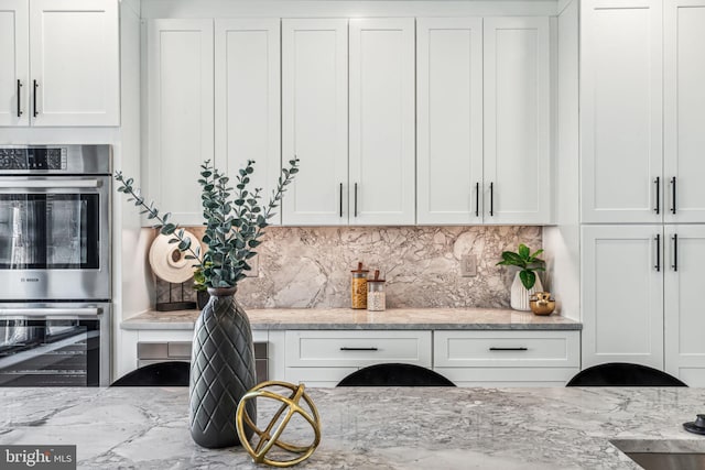 kitchen featuring light stone counters, stainless steel double oven, tasteful backsplash, and white cabinetry