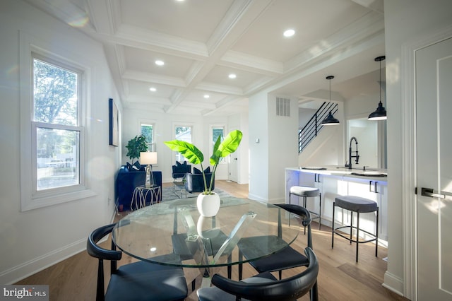 dining space with coffered ceiling, beamed ceiling, light hardwood / wood-style flooring, and sink