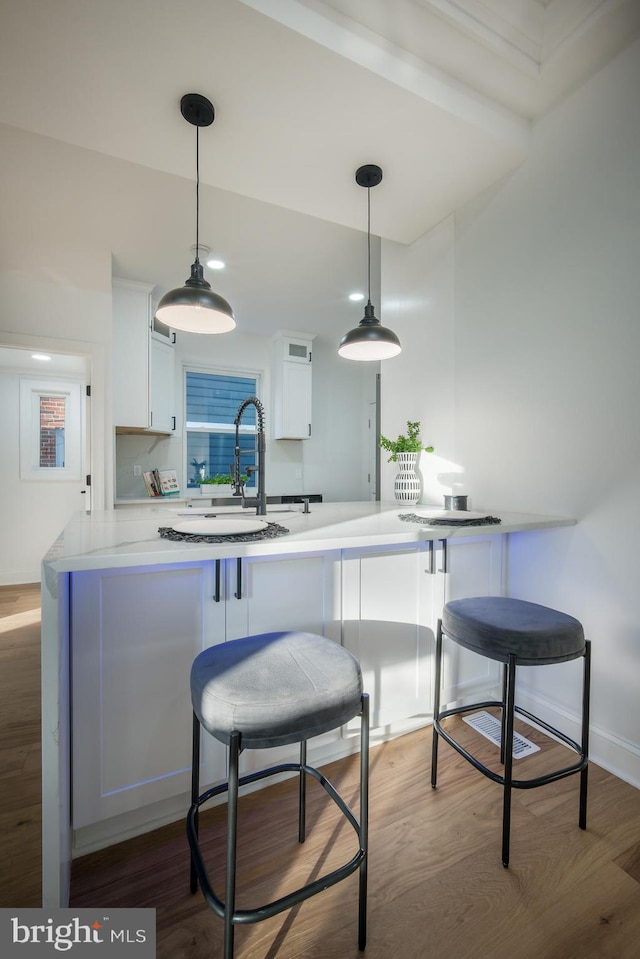 kitchen featuring white cabinetry, kitchen peninsula, hardwood / wood-style flooring, and hanging light fixtures