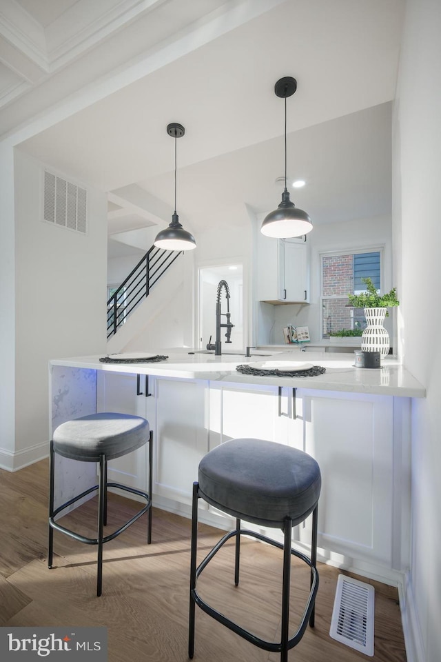 kitchen featuring hanging light fixtures, hardwood / wood-style floors, kitchen peninsula, and white cabinetry