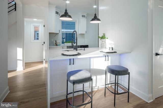 kitchen with light hardwood / wood-style floors, sink, white cabinets, kitchen peninsula, and a kitchen breakfast bar