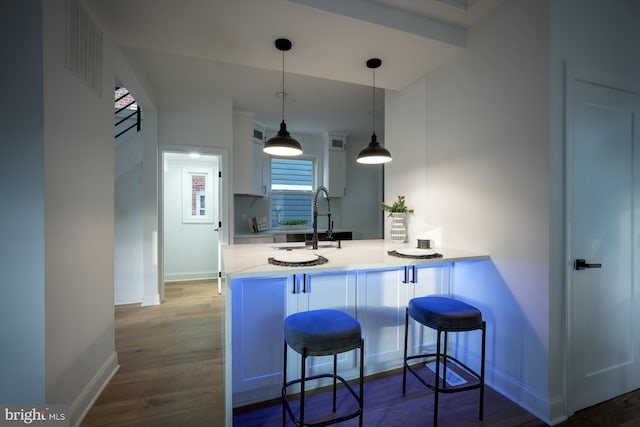 kitchen with sink, kitchen peninsula, decorative light fixtures, a kitchen breakfast bar, and hardwood / wood-style floors