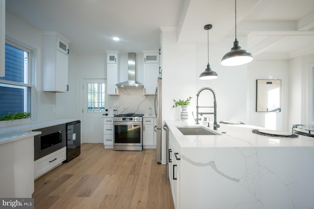 kitchen featuring pendant lighting, stainless steel appliances, white cabinetry, and wall chimney range hood