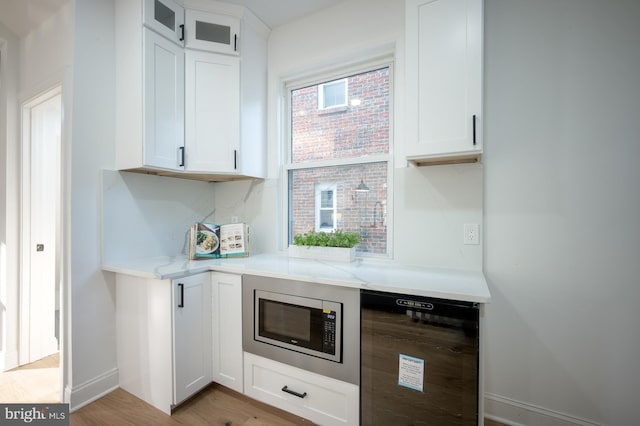 kitchen with beverage cooler, white cabinetry, stainless steel microwave, and light wood-type flooring