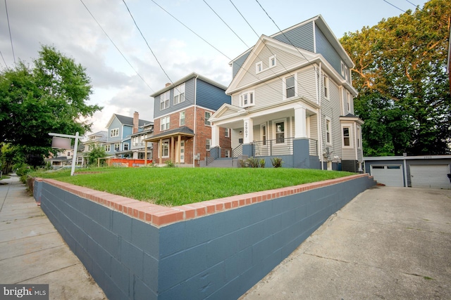 view of front of house featuring a garage, a porch, a front lawn, and an outbuilding