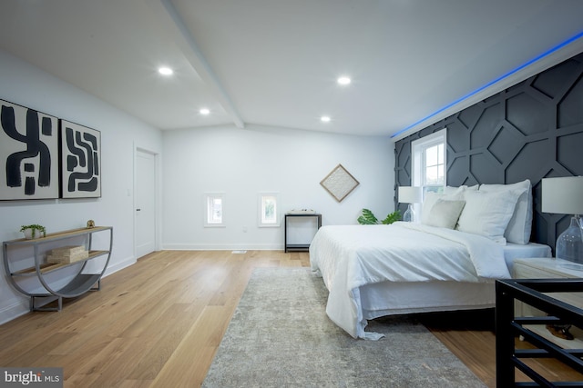 bedroom with lofted ceiling with beams and light wood-type flooring