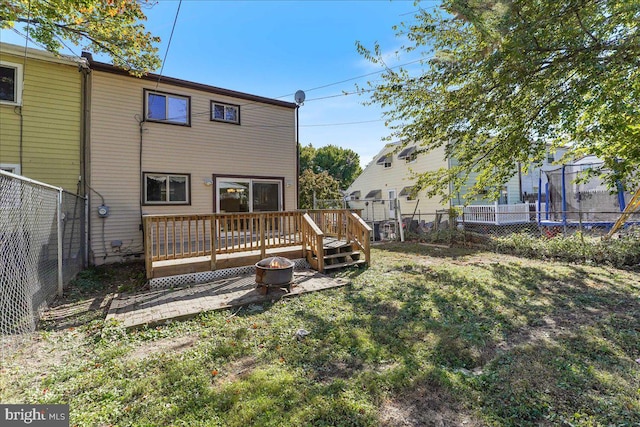 back of property featuring a lawn, a trampoline, and a wooden deck