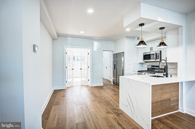 kitchen featuring pendant lighting, hardwood / wood-style flooring, kitchen peninsula, stainless steel appliances, and light stone countertops