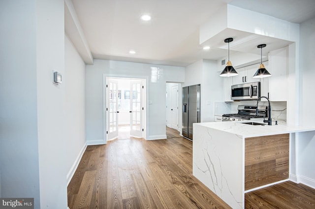 kitchen with sink, kitchen peninsula, decorative light fixtures, appliances with stainless steel finishes, and hardwood / wood-style floors