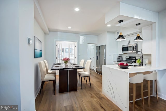 kitchen featuring kitchen peninsula, hanging light fixtures, a kitchen breakfast bar, stainless steel appliances, and hardwood / wood-style floors