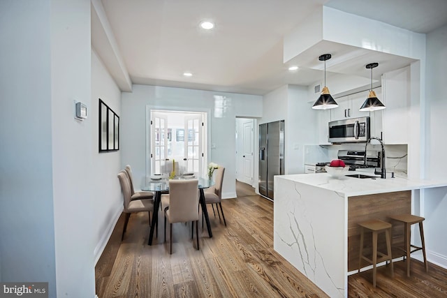 kitchen featuring appliances with stainless steel finishes, hanging light fixtures, white cabinets, kitchen peninsula, and dark hardwood / wood-style floors