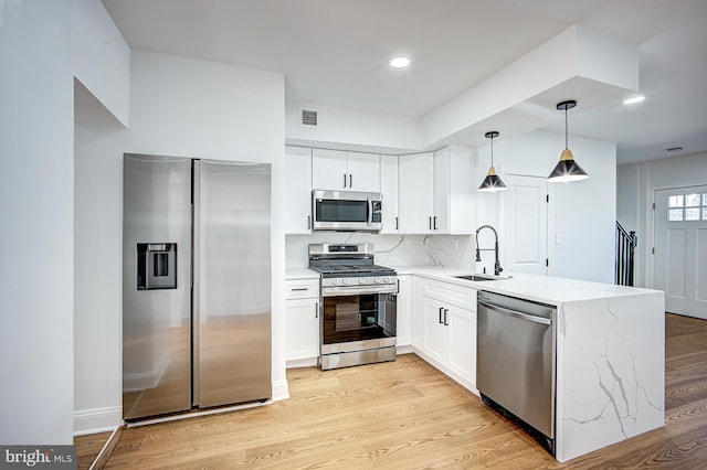 kitchen with white cabinets, hanging light fixtures, sink, light hardwood / wood-style flooring, and stainless steel appliances