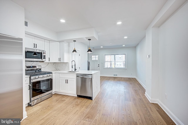 kitchen featuring pendant lighting, light wood-type flooring, sink, white cabinetry, and appliances with stainless steel finishes