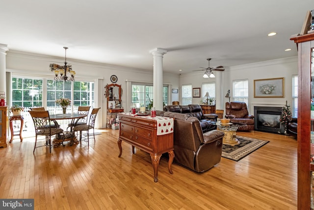 living room with ornamental molding, ceiling fan with notable chandelier, light wood-type flooring, and ornate columns