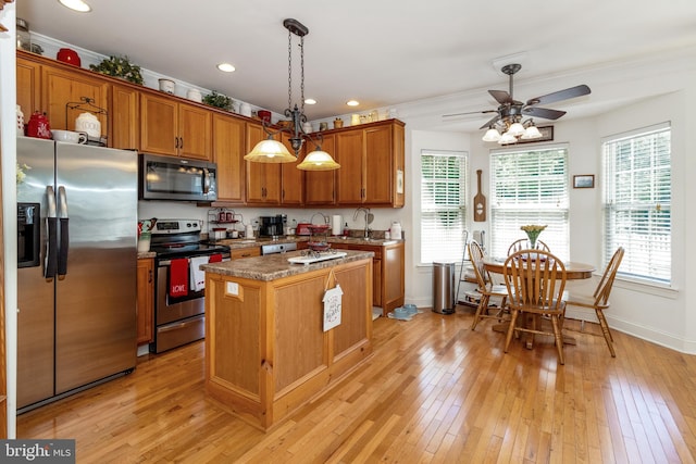 kitchen featuring pendant lighting, light hardwood / wood-style floors, a center island, ceiling fan with notable chandelier, and stainless steel appliances