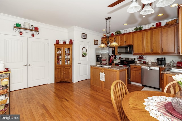 kitchen with appliances with stainless steel finishes, light hardwood / wood-style floors, a kitchen island, pendant lighting, and ornamental molding