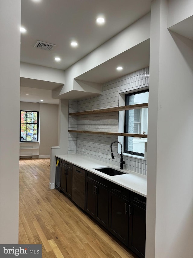 kitchen featuring sink, black dishwasher, light hardwood / wood-style flooring, dark brown cabinets, and backsplash