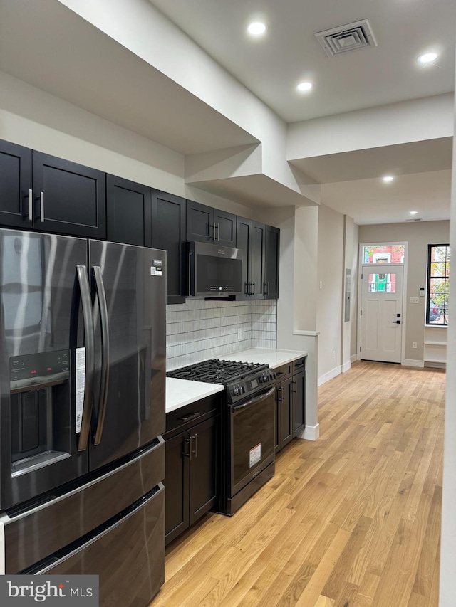 kitchen featuring appliances with stainless steel finishes, light wood-type flooring, and tasteful backsplash