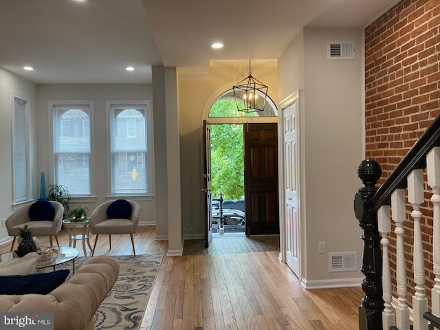 entryway with brick wall, an inviting chandelier, and light wood-type flooring