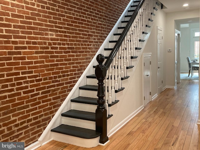 staircase with hardwood / wood-style flooring and brick wall