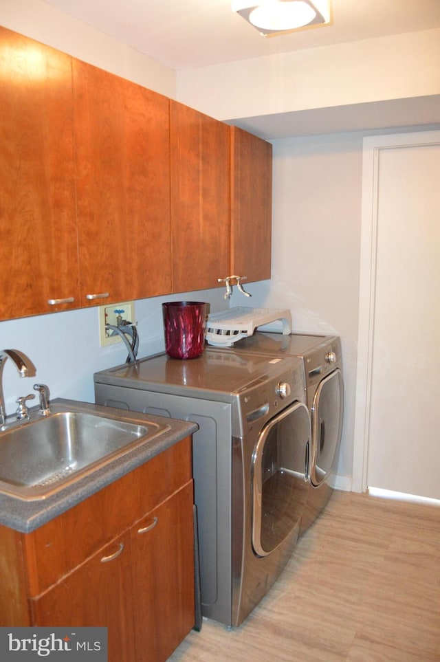 washroom featuring washer and clothes dryer, light hardwood / wood-style floors, sink, and cabinets