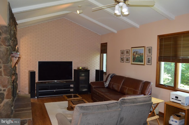 living room with ceiling fan, brick wall, dark wood-type flooring, lofted ceiling with beams, and a fireplace