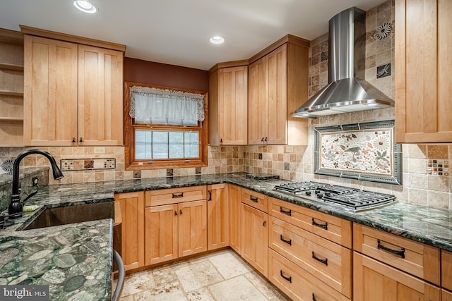 kitchen with dark stone counters, tasteful backsplash, sink, stainless steel gas cooktop, and wall chimney range hood