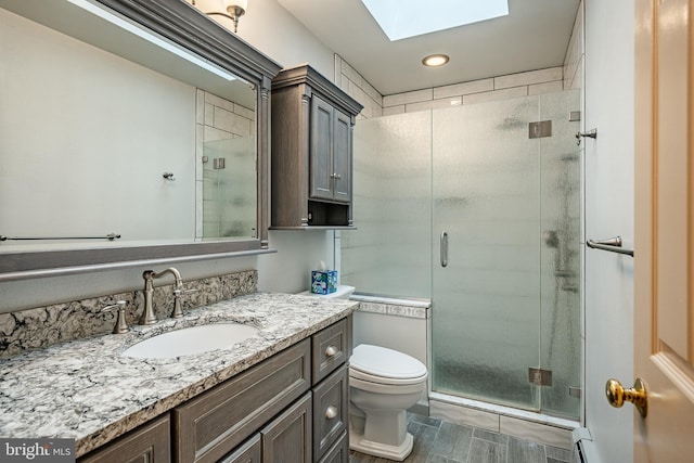 bathroom with vanity, toilet, a skylight, and a shower with shower door