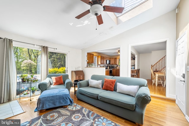 living room featuring vaulted ceiling with skylight, light hardwood / wood-style floors, and ceiling fan