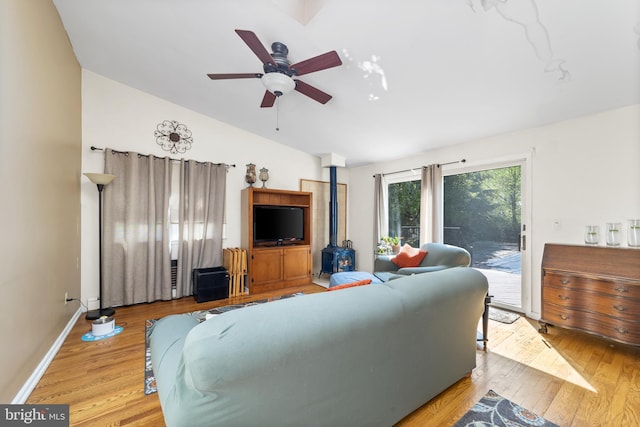 living room with light hardwood / wood-style flooring, a wood stove, vaulted ceiling, and ceiling fan