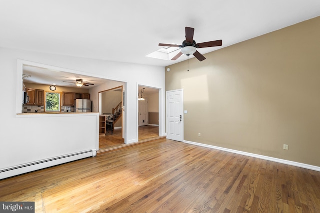 unfurnished living room featuring ceiling fan, lofted ceiling with skylight, light wood-type flooring, and baseboard heating