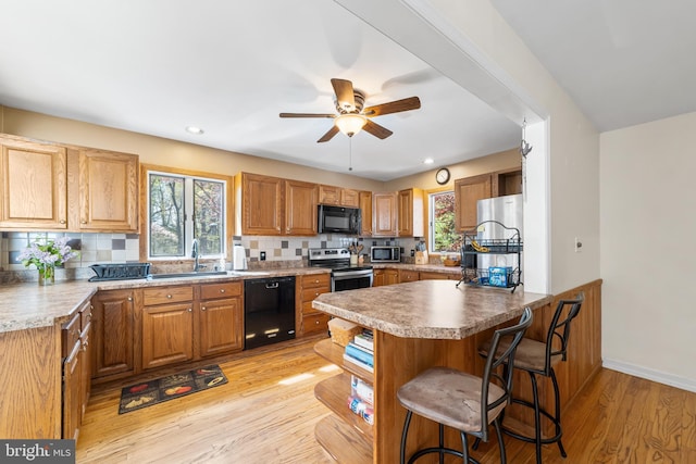 kitchen with sink, black appliances, a breakfast bar area, light wood-type flooring, and decorative backsplash